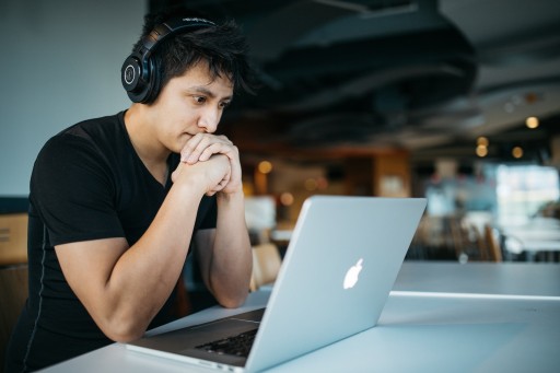 Tutoring: man wearing headphones while sitting on chair in front of MacBook